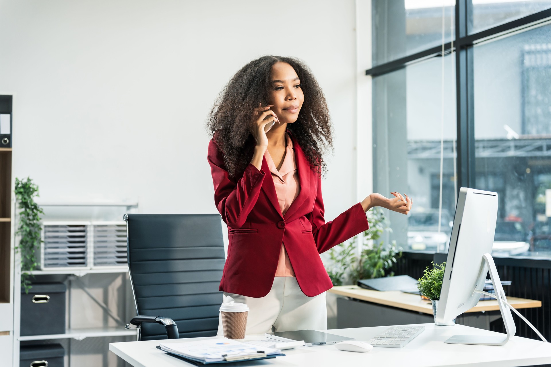An African American woman with an afro works at a wooden desk in an office, focusing on business finance for startup. She manages market research, scalability, and interacts with angel investors.